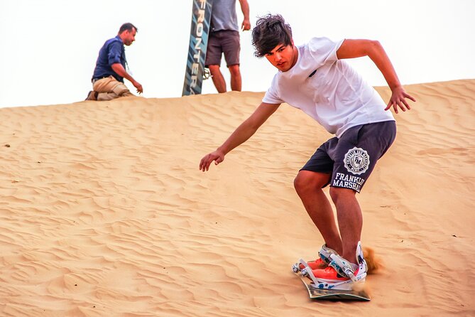 Dubai Private Sunset Desert Drive with Wildlife Experience - Learning sandboarding on an orange dune